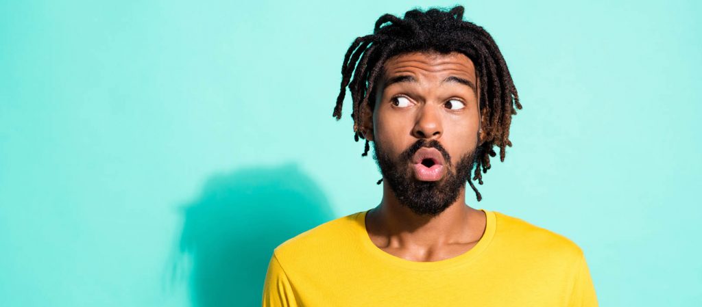 A man looks shocked, standing against a light blue background.