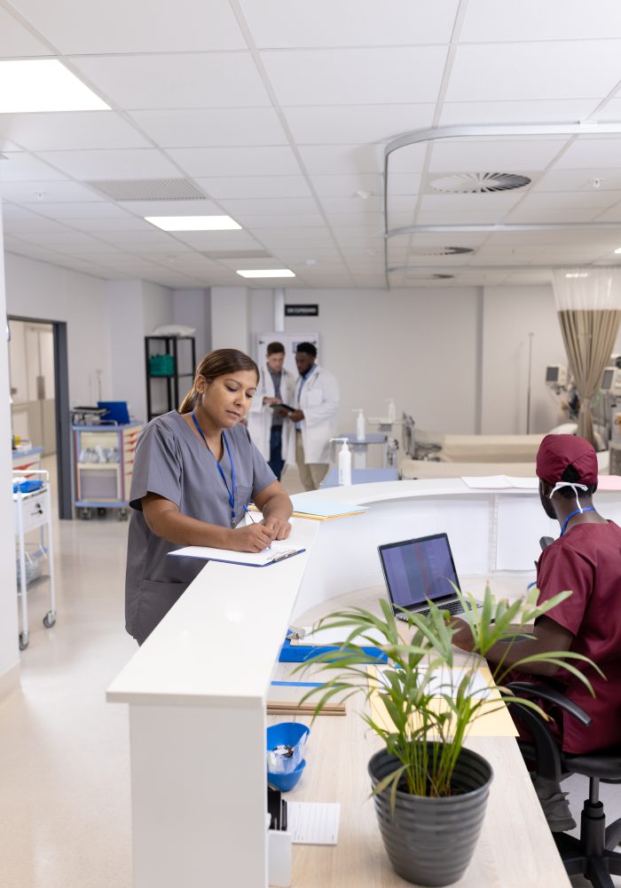 Asian female doctor writing on clipboard at reception desk of hospital ward, copy space. Hospital, medical and healthcare services.